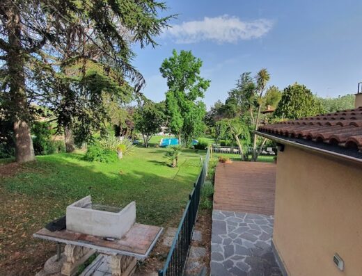 Giardino lussureggiante al Relais Villaggio Azzurro con piscina, alberi secolari e barbecue in pietra, un'oasi di relax e natura.