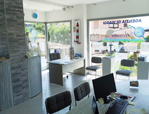 Interno luminoso di agenzia viaggi con scrivanie, sedie, computer e vetrine con logo. Agenzia di viaggi e tour operator specializzato in Sardegna, Sicilia e Corsica.