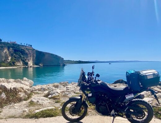 Noleggio moto a Palermo per tour in Sicilia: una moto da turismo con bauletto e accessori parcheggiata vicino alla costa con vista sul mare.