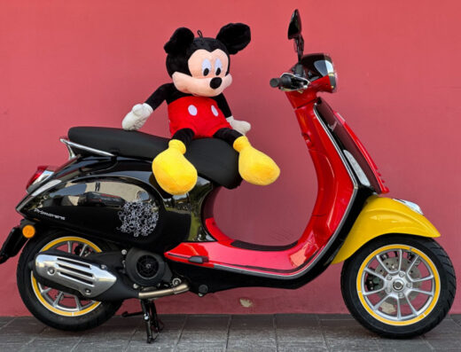 Noleggio scooter a Salerno: una Vespa Primavera bicolore (nera e rossa) con dettagli gialli e un pupazzo di Mickey Mouse sul sedile.