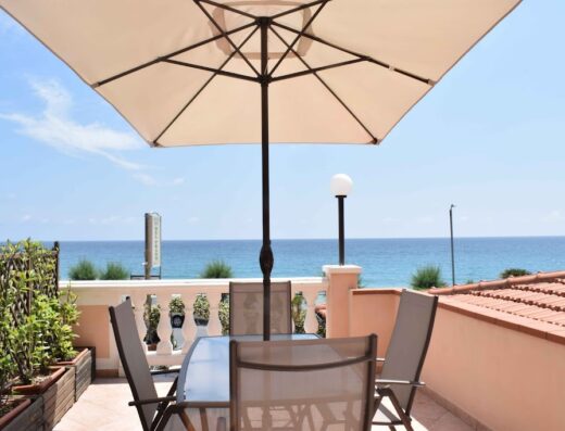 Terrazza panoramica al Residence del Prado con tavolo, sedie e ombrellone vista mare. Ideale per relax e vacanze.