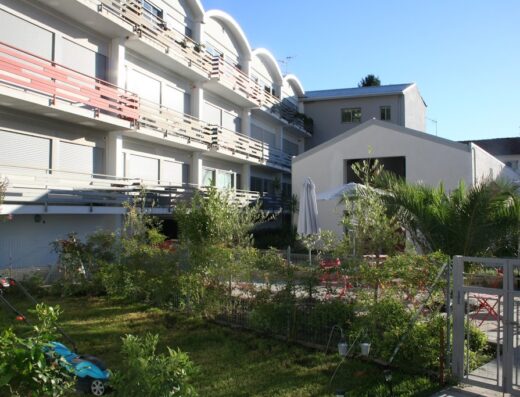 Residence Levante: vista esterna con prato verde curato, edificio con balconi e persiane chiuse, area relax con ombrellone e sedie rosse.