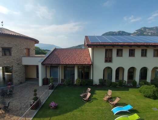 Vista aerea del Resort Monviso con edificio in pietra, pannelli solari, giardino con sedie a sdraio e montagne sullo sfondo.