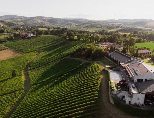 Vista aerea del Resort Opera02 immerso tra i vigneti italiani, con un paesaggio collinare sullo sfondo. Ideale per viaggi e relax.
