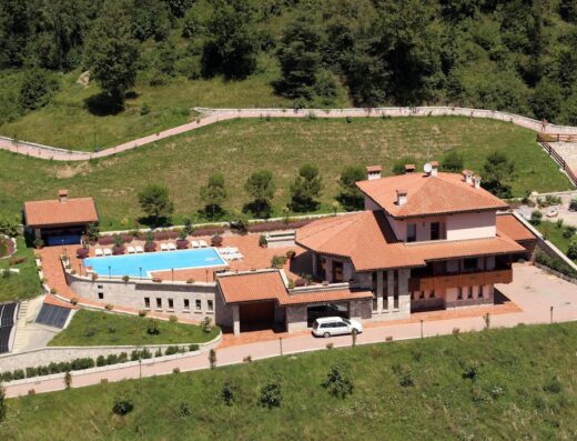 Vista aerea del resort San Pellegrino Terme con piscina, prato verde, alberi e parcheggio auto. Ideale per vacanze rilassanti e soggiorni benessere.