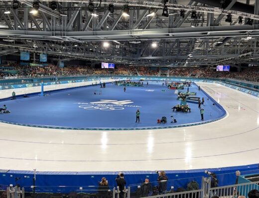 Panoramica dell'Oval di Torino, pista di pattinaggio su ghiaccio al coperto durante un evento sportivo con spettatori sulle tribune.