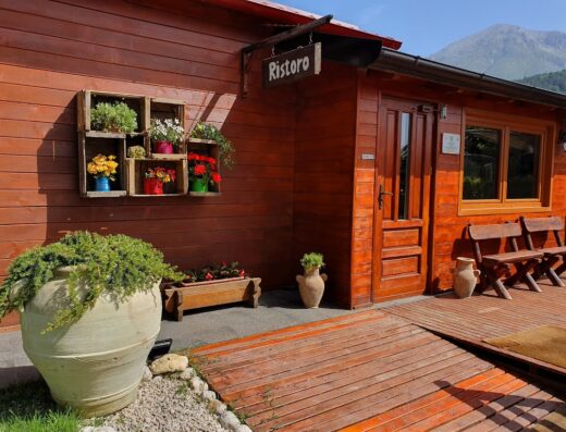 Ristorante Agriturismo Il Timo: Entrance view of the wooden building with flower decorations and mountain backdrop.