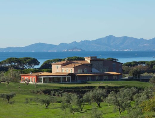 Vista panoramica del Riva Toscana Golf Resort & SPA, con edifici eleganti, campo da golf verdeggiante e mare sullo sfondo.