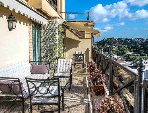 Balcone panoramico del River Palace Hotel a Roma con divanetto, sedie, tavolino, piante fiorite e vista sulla città.