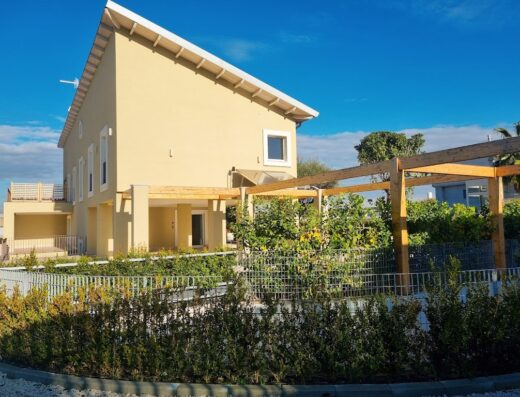 Ro agriMaison: Esterno di una casa a due piani con pergola in legno e giardino curato, cielo azzurro sullo sfondo.