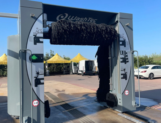 Autolavaggio Roelma: vista di un'attrezzatura WashTec per il lavaggio automatico di veicoli, con spazzole nere e indicazioni di sicurezza, situata all'aperto in una giornata soleggiata.