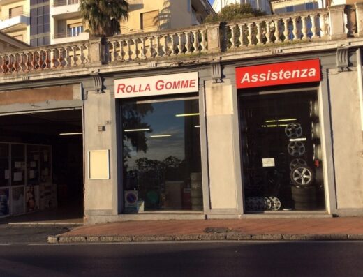 Rolla Gomme: Facciata di un negozio di pneumatici e assistenza per moto con insegne "Rolla Gomme" e "Assistenza". In vetrina si vedono cerchi e gomme per motocicli.