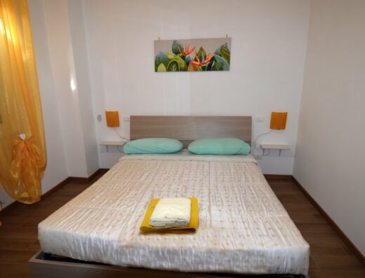 Camera da letto accogliente con letto matrimoniale, cuscini turchesi, asciugamani gialli, comodini con lampade arancioni e tenda dorata a Roma, perfetta per un soggiorno confortevole.