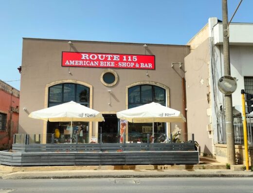 Route 115 American Bike Shop & Bar building exterior on a sunny day, showcasing motorcycles, accessories, and services for motorcycle enthusiasts.