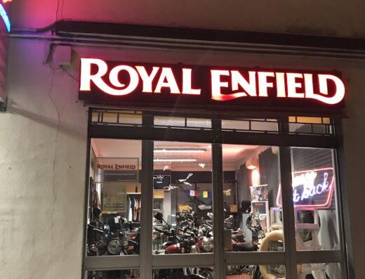 Vetrina illuminata di un concessionario Royal Enfield con diverse moto in esposizione, accessori e insegna luminosa del marchio.