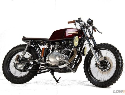 Una moto customizzata in stile retrò, con pneumatici tassellati, serbatoio bordeaux e dettagli artigianali, ideale per appassionati di moto d'epoca e viaggi avventura.