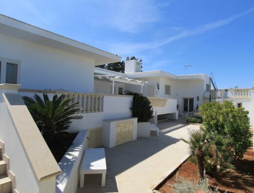Salenthouse: Esterno di una tipica casa salentina con muri bianchi, patio pavimentato, vegetazione mediterranea e cielo azzurro. Architettura tradizionale del Salento.