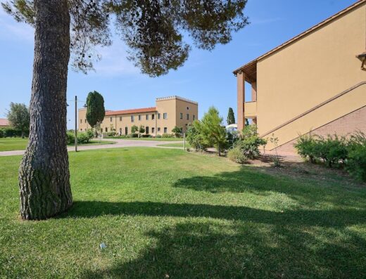 Salvapiano: Vista esterna di un edificio color ocra con prato verde curato, tipico dell'architettura toscana, in una giornata di sole.
