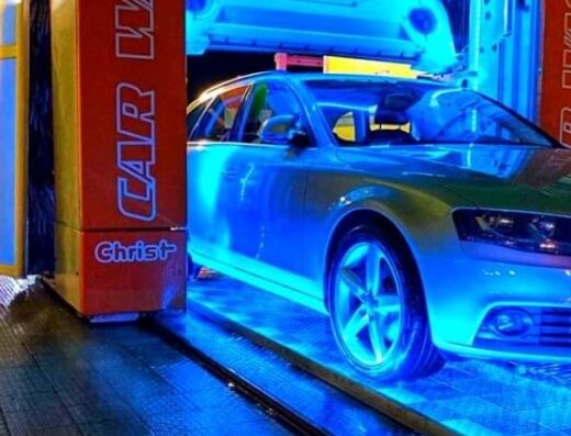 L'auto grigia entra nell'autolavaggio automatico Salvati Auto Wash Area a Latina, illuminata da luci blu durante il lavaggio.