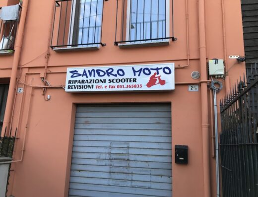 Sandro Moto: Facciata di officina specializzata in riparazioni scooter e revisioni, con insegna ben visibile e saracinesca chiusa.