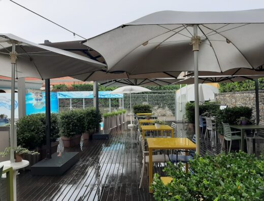 SanRemo Bike Hotel outdoor dining area with yellow tables and umbrellas, pool view, ideal for relaxing after a bike tour.