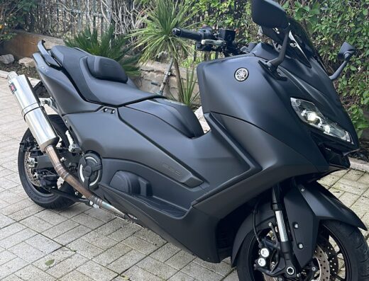 Saracino Motors: Elegante scooter Yamaha TMAX nero opaco parcheggiato su pavimentazione esterna, ideale per viaggi e spostamenti urbani con stile.