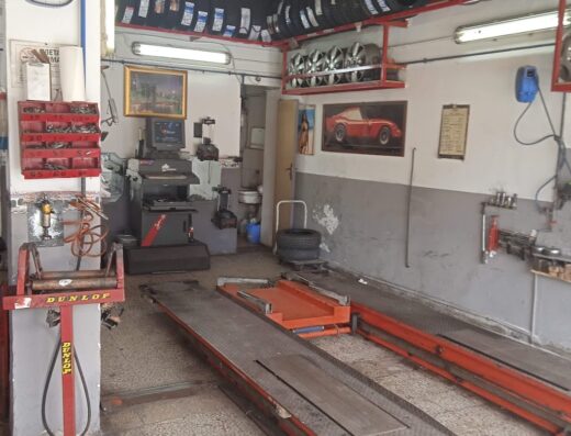 Interno dell'officina di Sartiano Giovanni, specializzata in servizi per moto e scooter. Si notano pneumatici, attrezzature per la riparazione e il controllo dei veicoli.