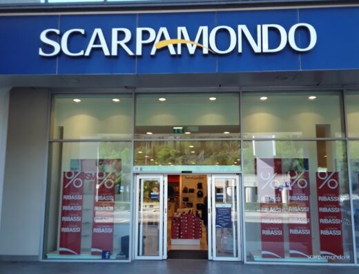 Scarpamondo store front with large glass windows, showcasing sale signs and displaying a variety of shoes and accessories inside.