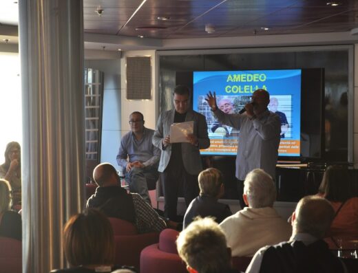 Presentazione di Scoop Travel Service S.r.l. con relatore che parla al microfono davanti al pubblico e schermo con il titolo Amedeo Colella.