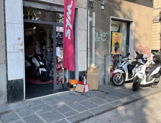 Negozio Scooter Point a La Spezia con scooter SYM in esposizione, bandiera del marchio e accessori in vendita. Servizi di riparazione e vendita scooter.