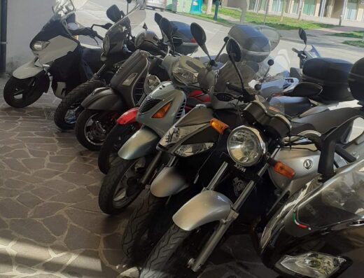 Esposizione di scooter e motocicli presso Scootermania di Busolin Stefano, con vari modelli parcheggiati per la vendita o la riparazione. Servizi di assistenza e vendita di accessori per moto disponibili.