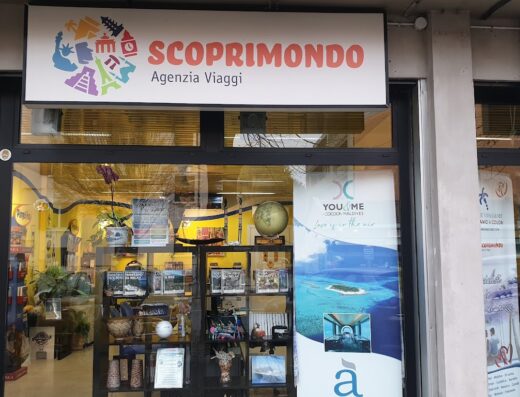 Vetrine dell'agenzia viaggi Scoprimondo, con insegna colorata e vetrina che espone cataloghi di viaggi, offerte vacanze e destinazioni esotiche