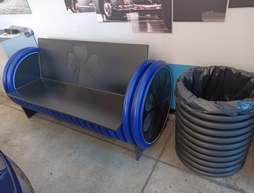 Arredamento insolito nell'officina Service Car Di Machina: una panca artigianale con ruote blu e un cestino dei rifiuti ricavato da un tubo corrugato.