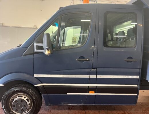 Servizio autolavaggio a mano: dettaglio della fiancata di un furgone blu scuro, pulito e lucido, con pneumatici bagnati.