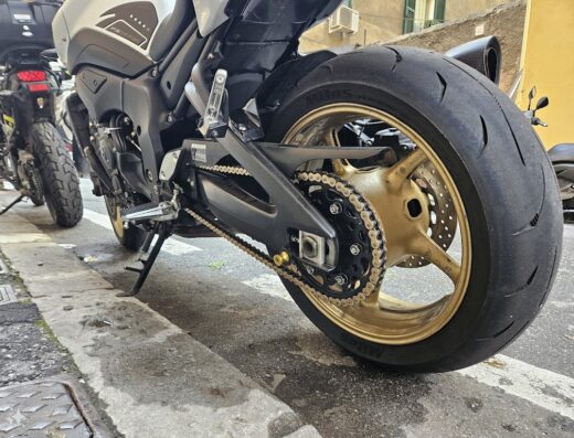 Dettaglio della ruota posteriore di una moto Yamaha con cerchio dorato, catena di trasmissione e pneumatico Mitas, parcheggiata a Sestri Levante.