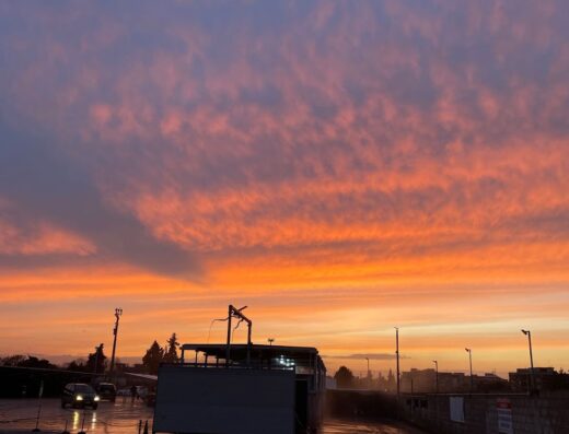 Tramonto infuocato su un'area di servizio con autolavaggio, auto in attesa e pavimentazione bagnata.