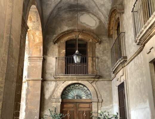 Cortile interno di un'agenzia di viaggi Shell con archi in pietra, balconi in ferro battuto, porta in legno massello e lampada a sospensione