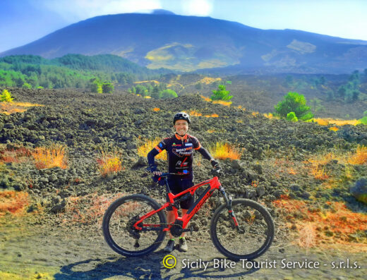 Escursionista in mountain bike elettrica di fronte al paesaggio lavico dell'Etna, Sicilia. Servizi turistici in bicicletta disponibili a Catania per tour ed escursioni.