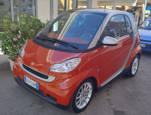 Auto Smart arancione parcheggiata di fronte a Silvio Clinic Car Detailing, in attesa di un servizio di pulizia e lucidatura professionale.