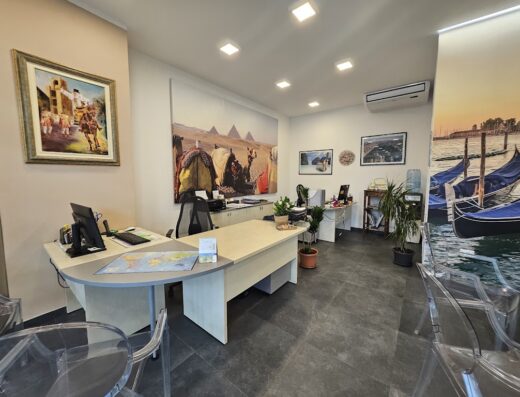 Interni di Sinis Viaggi: ufficio con scrivanie, computer, piante e immagini di viaggi esotiche e Venezia, agenzia di viaggi e servizi turistici
