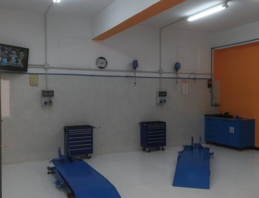 Interno di un'officina SMC Custom, con due ponti sollevatori blu, carrelli porta attrezzi, e pareti grigie. Servizio di personalizzazione e riparazione moto.