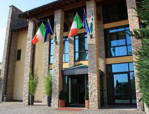 Sole della Franciacorta Hotel & Restaurant entrance with flags of Italy and Europe, stone pillars, and revolving door.