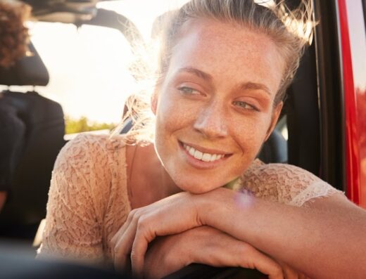 Donna sorridente appoggiata al finestrino di un'auto rossa, godendosi un viaggio su strada. Noleggio auto e servizi di viaggio.