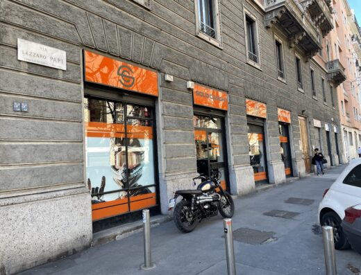 Solocaschi negozio di accessori moto a Milano, con una moto parcheggiata davanti e vetrine con immagini di caschi e motociclisti.