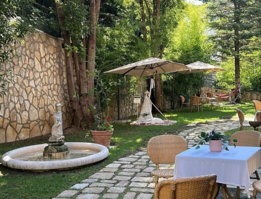 Raffinato giardino del Solofra Palace Hotel & Resort & Spa, con fontana, vialetto in pietra e tavoli per un'esperienza rilassante all'aperto.