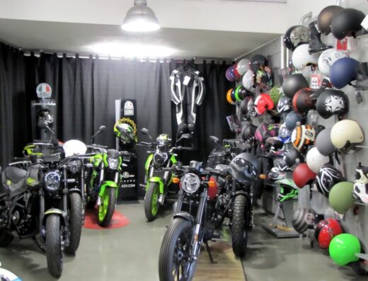 Interno di SP Motors con esposizione di moto nuove e usate, caschi da motociclista di vari colori e tute da moto in vendita.