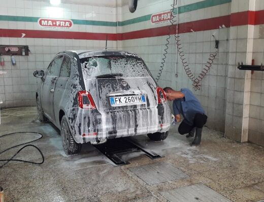 Auto speciale in fase di lavaggio presso un autolavaggio, con schiuma detergente e operatore al lavoro. Servizio professionale per cura auto.