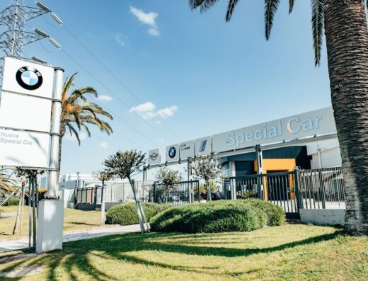 Concessionaria Special Car che vende BMW, MINI e BMW Motorrad con insegne ben visibili, circondata da palme e vegetazione in una giornata di sole.