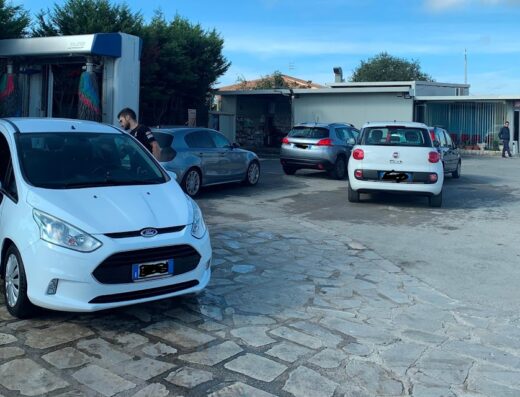 Diverse auto presso un autolavaggio self-service, con una Ford bianca in primo piano e altre vetture in attesa, riflettendo un'attività di cura e manutenzione veicolare.
