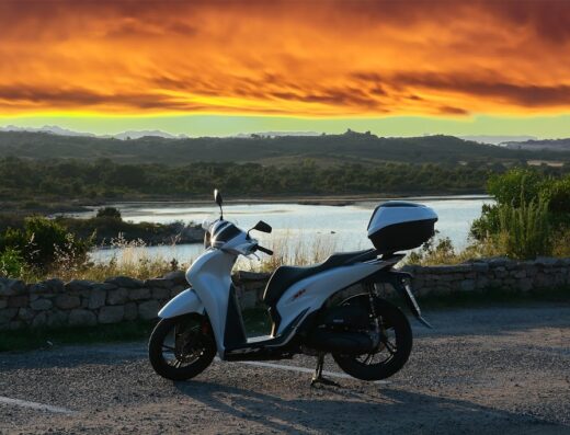 Noleggio scooter: SH bianca parcheggiata con bauletto, ideale per esplorare la costa al tramonto, servizio di mobilità su due ruote.